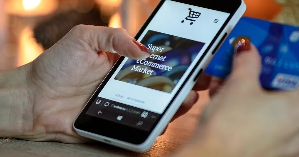Bir elinde telefon, diğerinde kredi kartıyla internetten alışveriş yapan biri