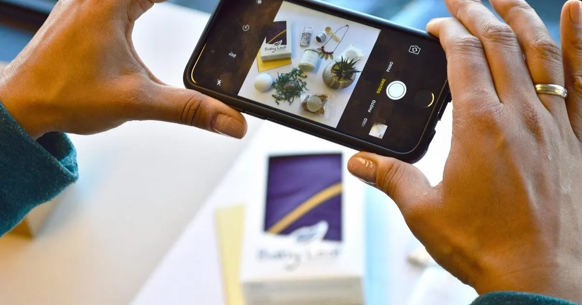Masadaki ürünlerin fotoğrafını telefonla çeken iki el